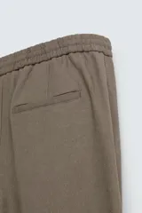Pantalón de calce relajado confeccionado en tejido de viscosa y yute color tostado. Presenta cintura elástica ajustable con cordón, bolsillos laterales, bolsillos traseros de vivo y cierre frontal con cremallera y botón.