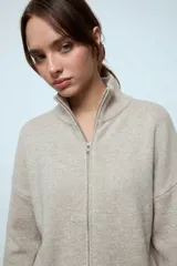 Cardigan de punto oversize en color beige, con cuello alto y cierre frontal completo de doble cursor. Presenta mangas largas con puños acanalados y un diseño holgado.