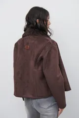Chaqueta tipo gamulán de color marrón, con solapas amplias forradas en corderito sintético oscuro. Presenta un diseño cruzado con botones frontales y mangas largas, ideal para un estilo invernal.