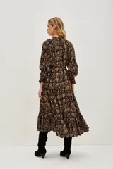 Vestido midi de corte fluido con estampado paisley en tonos oscuros, ocres y rosados. Presenta cuello redondo con lazo de ajuste, mangas largas abullonadas con puños elásticos y falda con volados en el ruedo.
