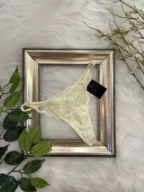 Tanga color crema con encaje floral y tiras finas regulables.