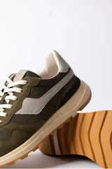 Championes urbanos de diseño técnico, combinando paneles de gamuza y tela en tono verde oliva con detalles en beige y negro. Presentan una suela de plataforma en color crema con base dentada en tono caramelo.