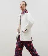 Campera acolchada de corte holgado, color blanco con diseño capitoneado en forma de rombos. Presenta cuello camisero y bordes internos con estampado floral en tonos azul y rojo, cierre frontal con botones a presión y bolsillos laterales.