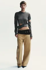 Jersey de punto gris oscuro, cuello redondo y manga larga. Presenta detalles desmontables con botones a lo largo de las costuras de las mangas y en el ruedo inferior.