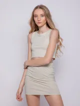 Falda corta color beige, tejida en tela brillante con textura acanalada y elástico en la cintura.