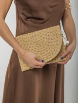 Cartera tipo sobre de rafia color beige con cierre de solapa y detalle de cuentas de madera en la correa de mano.