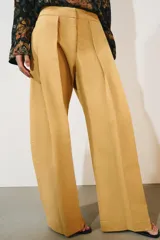 Jeans de tiro bajo y corte wide leg, color amarillo mostaza, con pliegues frontales, bolsillos ocultos y cierre frontal con cremallera, botón y ganchos metálicos.