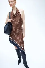 Vestido corto asimétrico de satén color marrón con lunares blancos, escote drapeado tipo halter y espalda descubierta. Cuenta con una franja ancha negra y rayas en la parte inferior.
