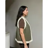 Chaleco estilo gamulán en color verde militar, con forro interior y bordes de corderito sintético en tono crema. Presenta un diseño sin mangas, ideal para usar sobre prendas de abrigo.