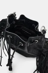 Bolso tipo saca color negro, de formato mini, con flecos laterales, cierre fruncido con cordones y correa combinada de cadena y tira de cuero sintético.