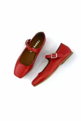 Zapato tipo Mary Jane color rojo, de cuero, con punta redondeada y tira sobre el empeine con hebilla metálica cuadrada.