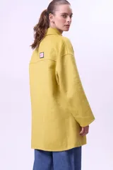 Tapado de lana color mostaza, de corte recto y diseño cruzado con botones frontales. Presenta solapas clásicas, mangas largas y bolsillos laterales.
