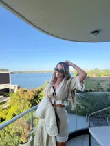 Top corto de lino color beige, con escote en V, cierre frontal con lazos y detalles de puntilla blanca en el escote, bajo y mangas.