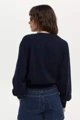 Sweater de tejido de punto color blanco marfil, con calce relajado, mangas largas levemente abullonadas, escote en V con botones y detalles de ribetes en color negro.