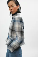 Blazer de corte peplum con cuello redondo y manga larga. Confeccionado en tejido de textura con mezcla de algodón y lino, presenta un estampado de cuadros en tonos azules y blancos. Incluye forro interior y cierre frontal mediante ganchos metálicos.