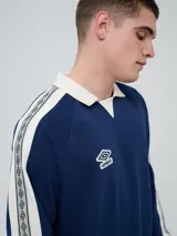 Buzo deportivo Umbro modelo Mixtape, color negro con cuello polo blanco y franjas blancas en las mangas con logo de la marca. Cuenta con puños y cintura elastizados.