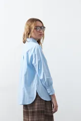 Camisa de corte relajado y diseño clásico, confeccionada en tela de algodón color celeste. Presenta cuello tradicional, cierre frontal con botones y mangas largas con puños rectos.