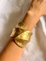 Brazalete rígido de diseño abierto, con acabado texturizado y efecto martillado en tono dorado mate.
