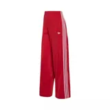 Pantalón deportivo Adidas Firebird Pinstripe de color rojo, con diseño de rayas diplomáticas verticales, corte ancho y pinzas en los laterales. Cuenta con las clásicas tres tiras blancas de la marca en los laterales y el logo del trifolio bordado en la parte frontal. Incluye bolsillos con cierre.