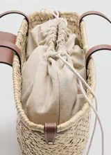Bolso de mano y hombro de fibra natural trenzada tipo paja, con detalles de cuero sintético marrón, doble asa de hombro, solapa frontal con cierre metálico dorado y forro interior de tela.