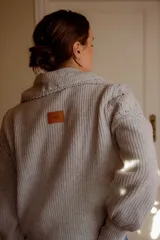 Sweater de punto color gris claro, con cuello amplio tipo solapa y detalles de tejido crochet en los hombros y mangas. Presenta mangas largas con puños ajustados y diseño de corte holgado.