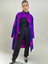 Tapado de lana merino afieltrada con diseño artesanal teñido en tonos violeta y fucsia. Presenta cuello elevado, cierre frontal con broches ocultos, bolsillos laterales y un corte ligeramente más largo en la parte trasera.