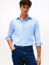 Camisa de manga larga Tommy Hilfiger en color celeste, con cuello clásico, cierre frontal de botones y logo de la marca bordado en el pecho. Presenta un corte regular y tejido técnico flexible.
