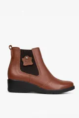 Bota de cuero color marrón, estilo botineta con taco chino negro, paneles elásticos laterales y detalle de aplique de cuero con grabado.