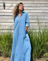 Vestido camisero largo de jean, con cierre frontal de botones, cuello camisero, mangas largas y detalle de volado en el ruedo.