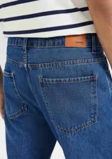 Pantalón de jean de corte slim, color azul clásico, con cierre de botón y cremallera, bolsillos laterales y traseros.