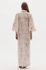 Vestido largo de lino con estampado floreado en tonos rosados, cuello camisero, botonadura frontal de nácar y mangas amplias abullonadas con puños elásticos. Presenta aberturas laterales en la falda.