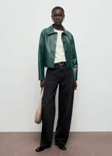Chaqueta corta de efecto piel en color verde, con cuello de solapa, cierre frontal de botones y dos bolsillos de parche con solapa en la parte delantera.