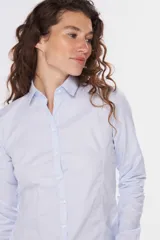Camisa de tejido Oxford lisa y color blanco, con cuello camisero, cierre frontal de botones y mangas largas con puños abotonados.