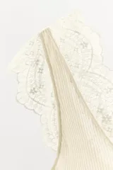 Top de punto acanalado en color beige, con escote en pico y tirantes anchos decorados con aplicaciones de encaje a tono.