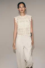 Blusa sin mangas confeccionada en tejido tipo crochet con diseño geométrico calado, cuello redondo y cierre frontal con botones.