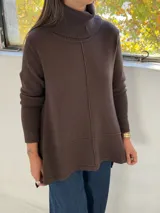 Sweater de punto color chocolate, con cuello alto acanalado, mangas largas y diseño holgado con costuras verticales y horizontales visibles.