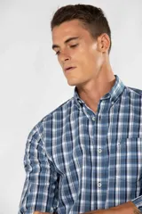 Camisa de manga larga con diseño de cuadros en tonos de azul, blanco y negro. Presenta cuello camisero con botones y un bolsillo ojal en el pecho con detalle bordado.