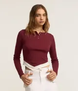 Blusa manga larga color borgoña confeccionada en rib con media vista de botones, manga larga y bajo asimétrica con detalle de tela blanca sobrepuesta.