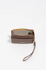 Monedero o tarjetero pequeño de cuero rojo, con cierre de cremallera superior y un tirador de tela a juego. Presenta un bolsillo exterior frontal y el logo de la marca grabado en dorado.