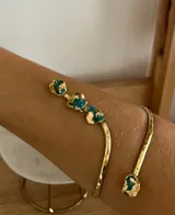 Brazalete abierto de metal dorado con acabado martillado, decorado con piedras naturales en tono turquesa con incrustaciones doradas en los extremos.
