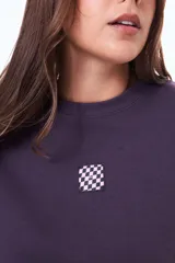 Buzo de felpa color negro con cuello redondo y ajuste holgado. Presenta un pequeño parche cuadrado con estampado a cuadros en el centro del pecho.