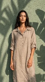 Vestido camisero midi de lino color beige, de calce relajado, con cuello clásico, cierre frontal parcial con botones, mangas 3/4 regulables y bolsillos delanteros.