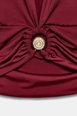 Top de poliamida color bordó con escote en pico, diseño sin mangas y detalle de drapeado frontal con fornitura metálica central.