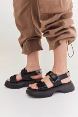Sandalias de plataforma con suela de goma negra y tiras de cuero sintético color beige con cierre de velcro ajustable.