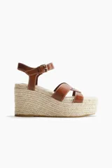Sandalias de tacón corrido con plataforma de yute trenzado, tiras de cuero marrón en el empeine y tira ajustable con hebilla en el tobillo.