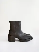 Bota corta de cuero negro con punta cuadrada y taco bloque texturizado. Presenta cierre lateral y costura central en el empeine.