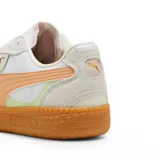 Championes Puma modelo Palermo, con diseño retro de perfil bajo. Presentan una combinación de cuero blanco y gamuza en tonos claros, con detalles en rosa pálido y una suela de goma color caramelo. Incluyen el logo de la marca en dorado en el lateral.
