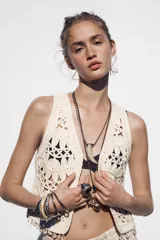 Chaleco abierto de punto color crudo con manga sisa y detalle de conchas en el ruedo.