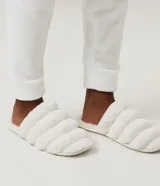 Pantufla cerrada de diseño acolchado con gajos, confeccionada en tejido de textura felpuda suave, con suela de goma termoplástica.