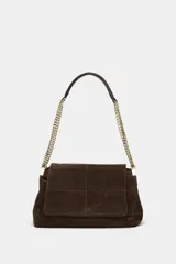 Bolso de hombro confeccionado en piel de ante color marrón, con diseño de pespuntes geométricos en la solapa. Cuenta con una correa de cadena metálica dorada y cierre imantado.